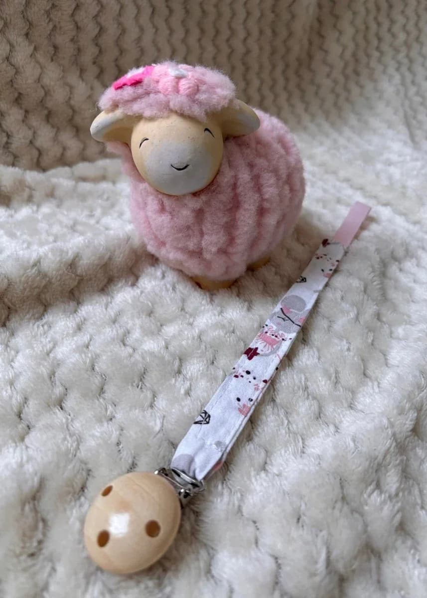 Bébé portant un gilet en tricot rose avec l'attache-tétine en tissu fixée à la tétine
