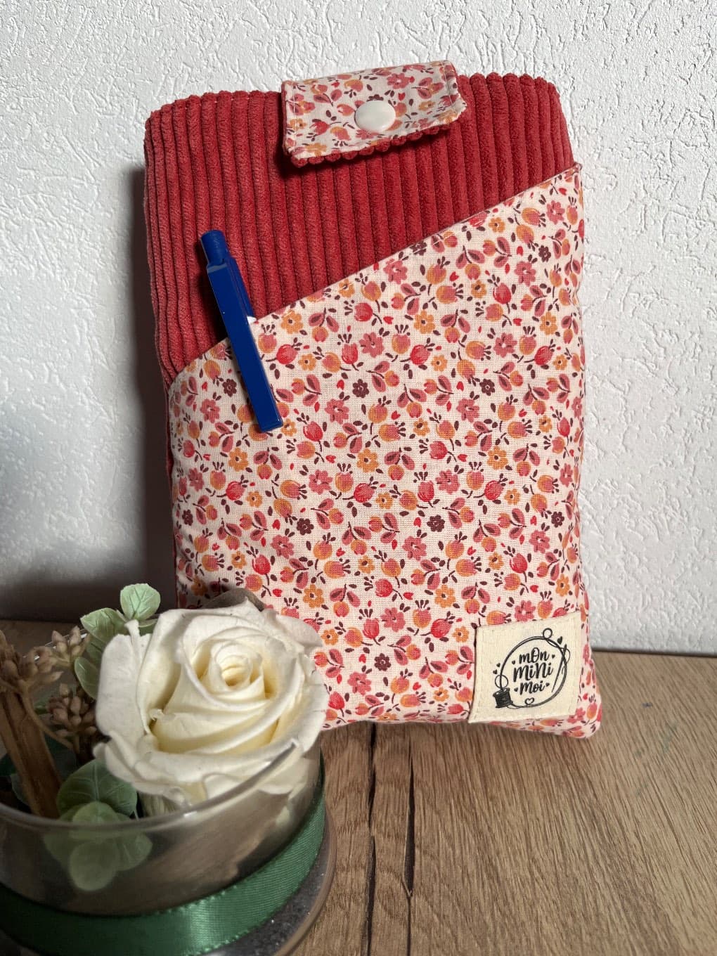 Pochette à livre rose et fleurie posée verticalement avec un stylo dans sa poche extérieure