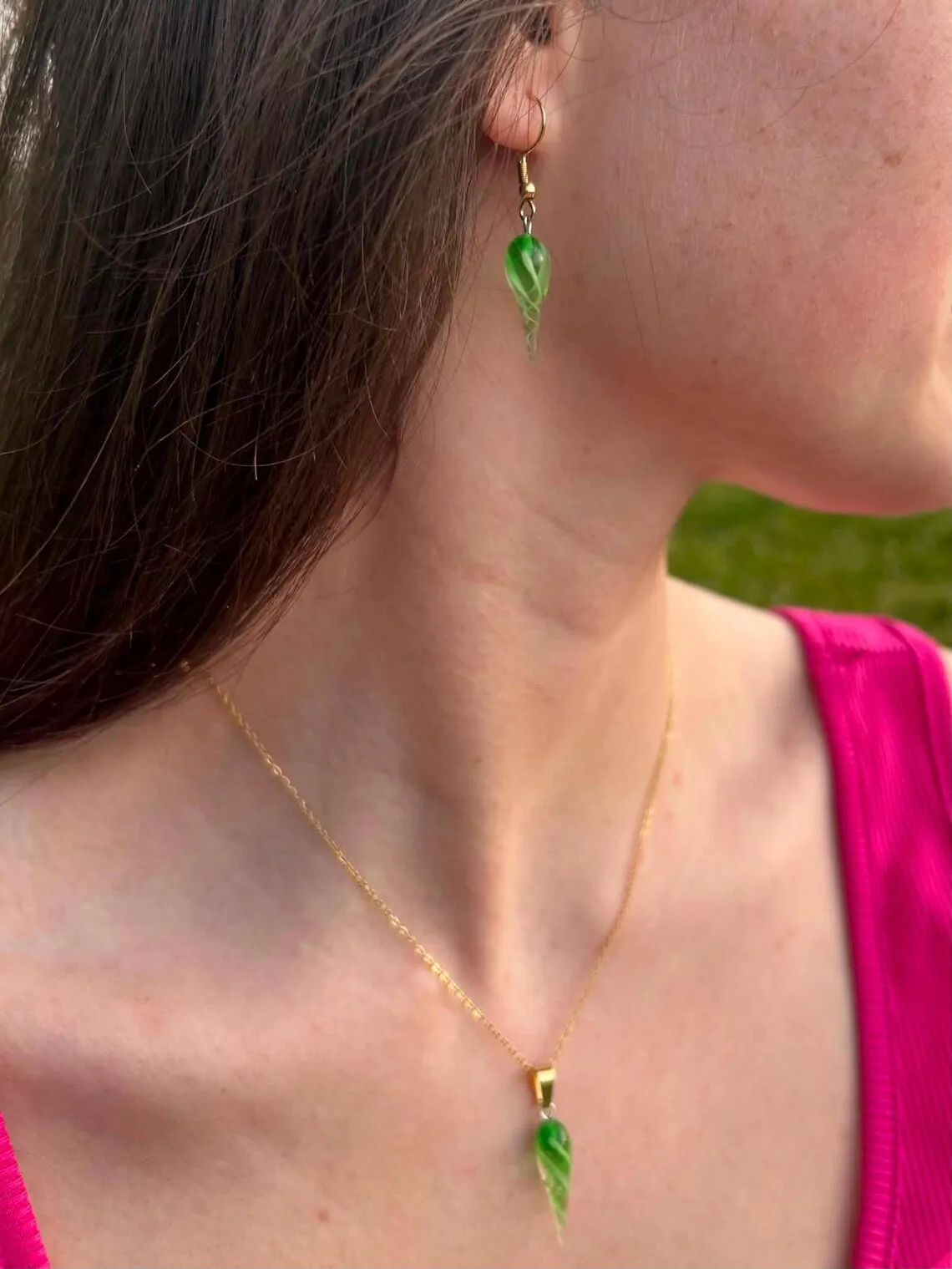 Boucle d'oreille pendante en verre vert torsadé portée à l'oreille, avec un pendentif assorti au cou.